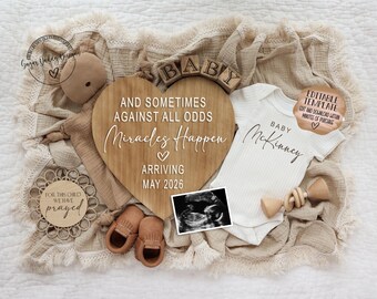 May include: A heart-shaped wooden sign with the text "AND SOMETIMES AGAINST ALL ODDS Miracles Happen ARRIVING MAY 2026". The image includes a baby onesie, ultrasound photo, baby shoes, and wooden blocks spelling "BABY".