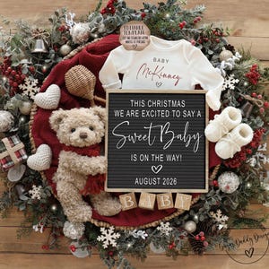 K&ouml;nnte beinhalten: Weihnachtliche Babyank&uuml;ndigung mit einem wei&szlig;en Strampler mit dem Namen "McKinney", einer Buchstaben-Tafel mit dem Text "Sweet Baby" und einem Teddyb&auml;ren. Die Ank&uuml;ndigung ist von einem dekorativen Kranz umgeben.
