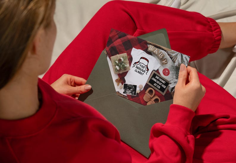 May include: An open olive green envelope revealing a pregnancy announcement. Inside, a onesie with the text "You Serious Clark?" is displayed alongside baby shoes, a sonogram, and a small sign.