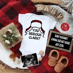 May include: A white baby onesie with the phrase "YOU SERIOUS CLARK?" and a red and black plaid hat design. The image includes baby shoes, a sonogram, and a sign that reads "BABY MCKINNEY JOINING OUR NUT HOUSE JULY 2026."