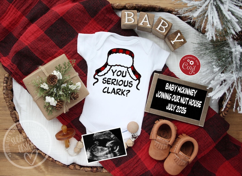 May include: A white baby onesie with the phrase "YOU SERIOUS CLARK?" and a red and black plaid hat design. The image includes baby shoes, a sonogram, and a sign that reads "BABY MCKINNEY JOINING OUR NUT HOUSE JULY 2026."