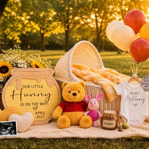 May include: A Winnie the Pooh themed baby announcement set featuring a yellow honey pot letter board with the text Our Little Hunny Is On The Way April 2027, a plush bear and piglet, a white baby bodysuit, a honey jar, and a wicker bassinet.