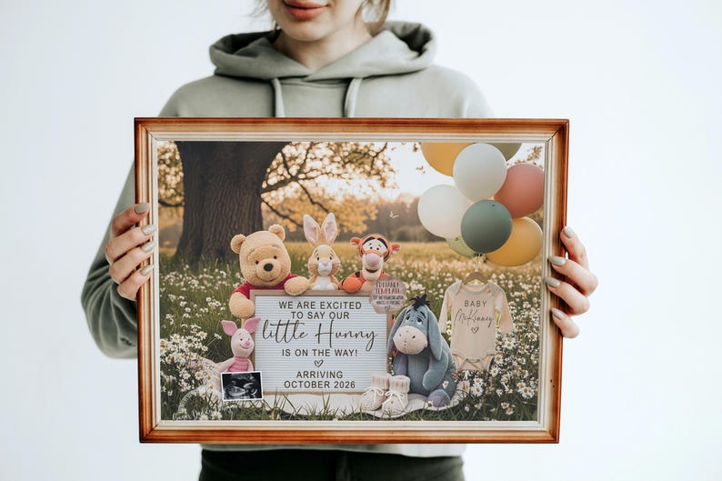 May include: A framed announcement featuring Winnie the Pooh characters, balloons, and baby clothes. The sign reads "We are excited to say our little Hunny is on the way! Arriving October 2026."