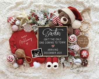 May include: A Christmas pregnancy announcement. A red babygrow with "Baby McKinney" printed on it, a letter board with the text "Santa isn't the only one coming to town! Arriving December 2024", and a teddy bear wearing a Santa hat. Decorations include baubles and foliage.