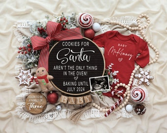 Könnte beinhalten: Eine Weihnachts-Schwangerschaftsanzeige mit einem schwarzen Buchstabenbrett, auf dem steht "Cookies for Santa aren't the only thing in the oven! Baking until July 2024".  Ein roter Strampler mit dem Text "Baby McKinney" ist im Bild enthalten.  Das Bild enthält auch ein Holzschild mit der Aufschrift "Soon to be a family of three".