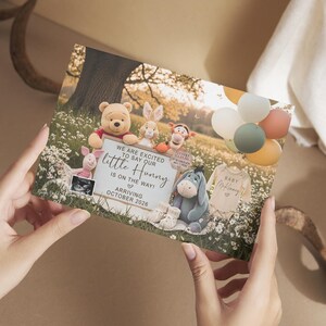 May include: A baby announcement card featuring Winnie the Pooh characters. The card includes the text "We are excited to say our little Hunny is on the way! Arriving October 2026." Balloons and a baby onesie are also visible.