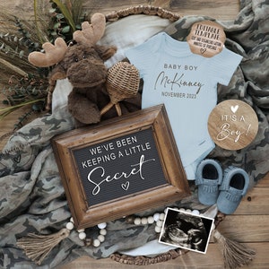 May include: A baby announcement with a blue onesie, a wooden sign that says "It's a Boy!" and a framed sign that says "We've been keeping a little secret".