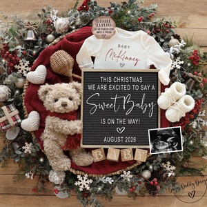 K&ouml;nnte beinhalten: Weihnachtliche Schwangerschaftsank&uuml;ndigung. Ein wei&szlig;er Baby-Body mit dem Namen "McKinney" und eine Buchstaben-Tafel mit der Aufschrift "Sweet Baby is on the way! August 2026." Die Ank&uuml;ndigung enth&auml;lt einen Teddyb&auml;ren, Babyschuhe und ein Ultraschallbild, umgeben von Dekorationen.