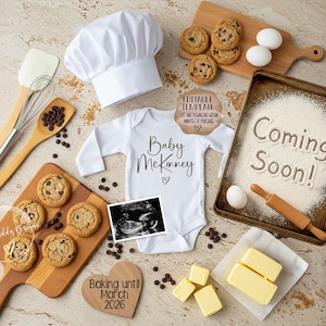 May include: A charming pregnancy announcement featuring baking-themed elements. Includes a white onesie with "Baby Mckinney" text, a chef's hat, cookies, eggs, butter, and a tray with "Coming Soon!" written in flour. A sonogram image is also present.