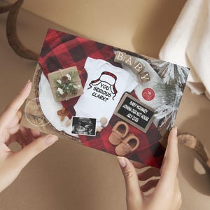May include: A pregnancy announcement card with a white onesie featuring a Santa hat design and the text "YOU SERIOUS CLARK?". The card includes baby shoes, a sonogram, and a small gift box on a red and black plaid background.