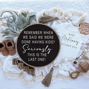 May include: A black letter board with the text "Remember when we said we were done having kids? Seriously this is the last one!"  A white onesie with the text "Baby McKinney October 2023" is next to the letter board.  There are brown moccasins, wooden blocks that spell "baby", and a wooden rattle.
