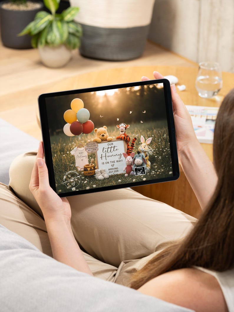 May include: A tablet displays a pregnancy announcement with Winnie the Pooh characters. The announcement includes a sign that reads "Our Little Hunny is on the way!" with the expected arrival date of July 2025. Balloons and baby clothes are also visible.