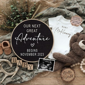 May include: A black letter board with the text "Our next great adventure begins November 2023". A white onesie with the text "Baby McKinney" is next to the letter board. There are brown baby booties, a wooden block that says "Baby", a teddy bear, a wooden sign that says "Hello World", and an ultrasound image.
