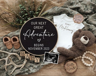 May include: A black letter board with the text "Our next great adventure begins November 2023". A white onesie with the text "Baby McKinney" is next to the letter board. There are brown baby booties, a wooden block that says "Baby", a teddy bear, a wooden sign that says "Hello World", and an ultrasound image.