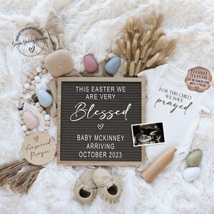 May include: A pregnancy announcement with a letter board that reads "This Easter we are very blessed. Baby McKinney arriving October 2023". There is a small ultrasound image, a white onesie with the text "For this child we have prayed", and a wooden sign that says "Answered Prayer".