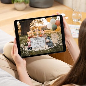 May include: A tablet displays a baby announcement with Winnie the Pooh characters. The announcement includes the text "We are excited to say our little Hunny is on the way! Arriving October 2026."