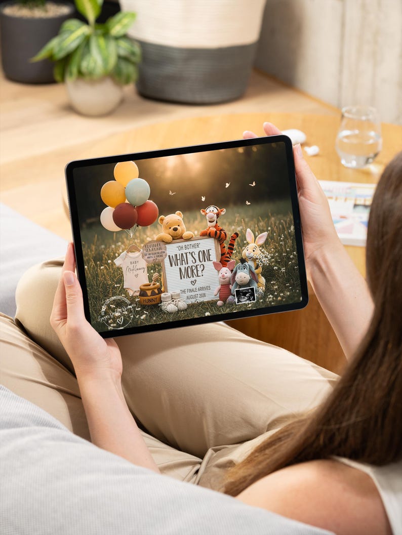 May include: A tablet displays a pregnancy announcement featuring Winnie the Pooh characters. The announcement includes a sign that reads "What's One More?" with the expected arrival date. Balloons and baby clothes are also visible.