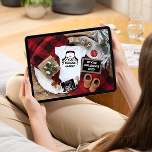 May include: A tablet displays a pregnancy announcement with a white onesie that says "You Serious Clark?" and a Santa hat graphic. The announcement includes baby shoes, a sonogram, and the text "Baby McKinney Joining Our Nut House July 2026."