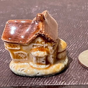 May include: A brown ceramic figurine of a small house with a brown roof and a sign that reads "Jack Mock".