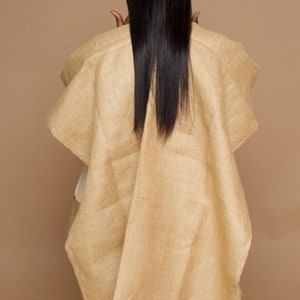 Op de afbeelding: Een beige poncho met franjes. De poncho is gemaakt van geweven stof en heeft een losse, vloeiende pasvorm.