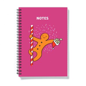 May include: A pink spiral bound notebook with the word "NOTES" printed on the front. The cover features a cartoon gingerbread man holding a bag of money and hanging from a candy cane pole.