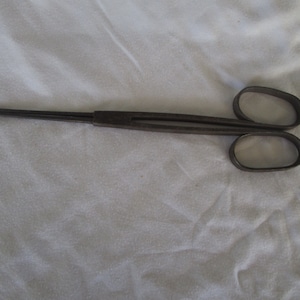 May include: A pair of antique metal tongs with long handles and a simple design. The tongs are made of dark metal and have a slightly rusted finish.