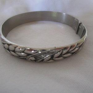 May include: A silver bangle bracelet with a wheat design. The bracelet is made of metal and has a hinged clasp.