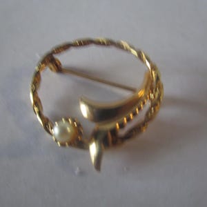 May include: A gold-toned brooch with a twisted wire design and a single pearl accent.