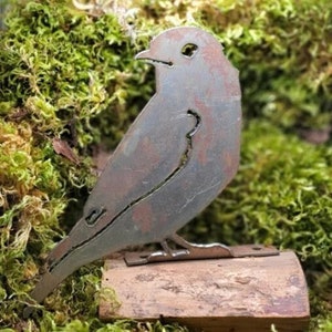 May include: A rusty metal bird sculpture with a brown wooden base. The bird is perched on the base and has a detailed design.