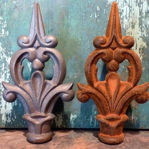 May include: Two ornate metal finials, one with a silver finish and the other with a rusty brown finish. Both finials feature a decorative, stylized floral design.