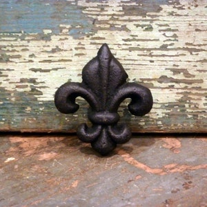 May include: A black cast iron fleur-de-lis design. The design is on a rustic wooden background.