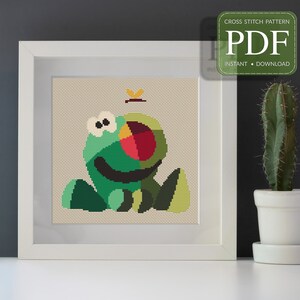 Puede incluir: Patrón de punto de cruz en formato PDF para descargar, que representa una rana verde, roja y amarilla con una mariposa encima. La rana está sentada sobre una hoja verde.