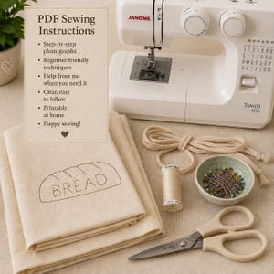 May include: A white Janome Sewist 525S sewing machine, a stack of beige fabric with a bread outline and text, a spool of beige thread, a small bowl of colorful sewing pins, a length of beige cord, and beige-handled scissors with metal blades.