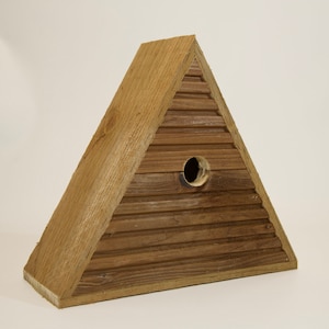 May include: A triangular wooden birdhouse with a round entrance hole. The birdhouse is made of natural wood with a rustic finish.