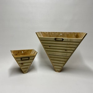 May include: Two wooden triangular wall planters with a rustic finish. The larger planter is 30 cm tall and the smaller planter is 15 cm tall. Both planters have a metal handle.