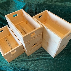 May include: Four wooden crates stacked on top of each other. The crates are made of natural wood and have a rustic look. The crates are all the same size and have handles on the sides.