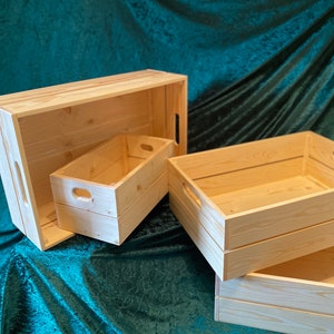 May include: Three wooden crates of varying sizes, made from natural light wood. The crates are stacked on top of each other, with the largest crate at the bottom and the smallest crate on top. The crates have a rustic, farmhouse style.