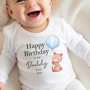 Peut inclure: Combinaison blanche pour b&eacute;b&eacute; avec un ballon bleu qui dit "1er" et un ours brun tenant le ballon. La combinaison dit "Joyeux anniversaire en tant que mon papa Amour Arlo".
