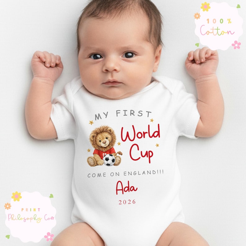May include: White baby bodysuit with the text "MY FIRST World Cup" in red, featuring a lion holding a football. The bodysuit also includes the name "Ada" and the year "2026".