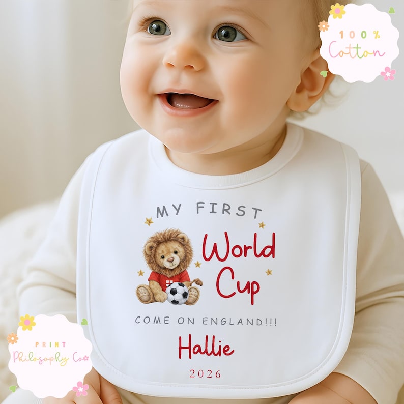 May include: A white baby bib featuring the text "MY FIRST World Cup" in red, a lion illustration, the name "Hallie", and the year "2026". The bib is made of 100% cotton. The text "COME ON ENGLAND!!!" is also visible.