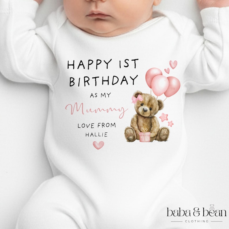 Pode incluir: Um body branco de manga comprida para beb&eacute; com uma ilustra&ccedil;&atilde;o de um urso de peluche castanho com um la&ccedil;o cor-de-rosa, bal&otilde;es cor-de-rosa e estrelas. O texto diz: HAPPY 1ST BIRTHDAY AS MY Mummy LOVE FROM HALLIE. Inclui cora&ccedil;&otilde;es e um presente.