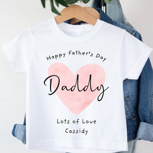May include: White t-shirt with a pink watercolor heart that says "Daddy" inside. The text "Happy Father's Day" is above the heart and "Lots of Love Cassidy" is below the heart.