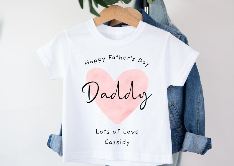 May include: White t-shirt with a pink watercolor heart that says "Daddy" inside. The text "Happy Father's Day" is above the heart and "Lots of Love Cassidy" is below the heart.