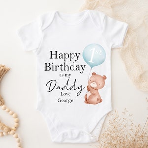 Peut inclure: Combinaison blanche pour b&eacute;b&eacute; avec le texte "Happy 1st Birthday as my Daddy Love George" et un ours en dessin anim&eacute; tenant un ballon bleu avec le num&eacute;ro 1 dessus.