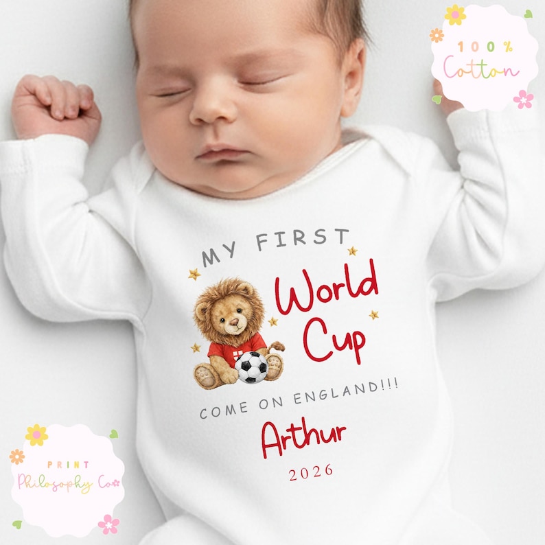May include: A white baby bodysuit with long sleeves. It has the text "MY FIRST World Cup" in red, a lion illustration with a football, and the name "Arthur". The text "COME ON ENGLAND!!!" and the year 2026 are also printed on the bodysuit.
