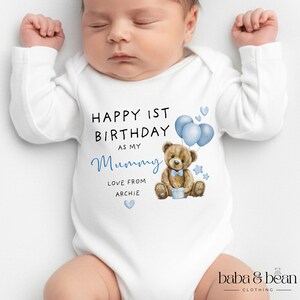 Pode incluir: Um body branco de manga comprida para beb&eacute; com uma ilustra&ccedil;&atilde;o de um urso de peluche castanho com bal&otilde;es azuis, uma gravata borboleta azul e um presente. O texto diz: HAPPY 1ST BIRTHDAY AS MY Mummy LOVE FROM ARCHIE, com cora&ccedil;&otilde;es e estrelas.