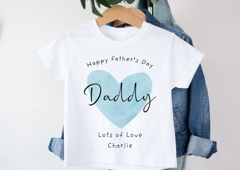 May include: White t-shirt with a blue watercolor heart that says "Daddy" inside. The text "Happy Father's Day" is above the heart and "Lots of Love Charlie" is below the heart.