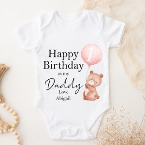 Peut inclure: Combinaison blanche pour b&eacute;b&eacute; avec le texte "Happy Birthday as my Daddy Love Abigail" et un ballon rose avec le chiffre 1 dessus. Un ours brun avec un nez rose tient le ballon.