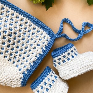 May include: A set of crocheted baby booties and a matching hat. The booties and hat are white with a blue trim. The hat has a tie.
