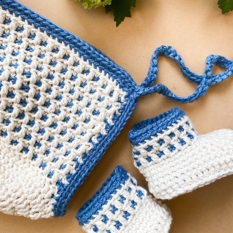 May include: A set of crocheted baby booties and a matching hat. The booties and hat are white with a blue trim. The hat has a tie.
